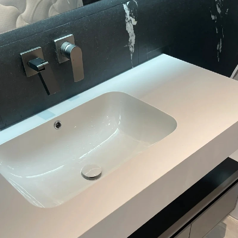 Custom-designed white rectangular undermount ceramic sink seamlessly integrated with a luxury stone countertop for a bespoke bathroom project.